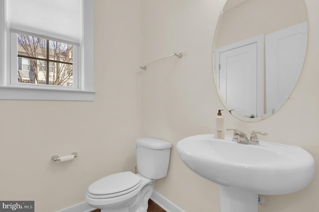 half bath with baseboards, a sink, and toilet