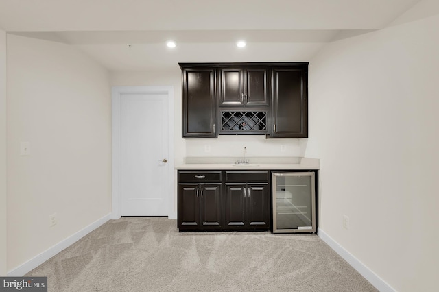 bar with wine cooler, indoor wet bar, light carpet, a sink, and baseboards