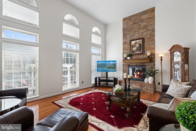 living area featuring a fireplace, a high ceiling, wood finished floors, and baseboards