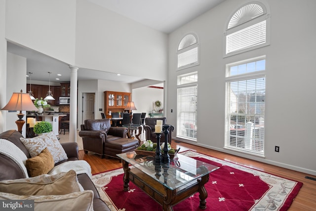 living area with visible vents, wood finished floors, decorative columns, baseboards, and a towering ceiling