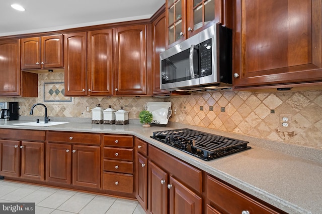 kitchen featuring black gas stovetop, a sink, stainless steel microwave, light tile patterned flooring, and light countertops