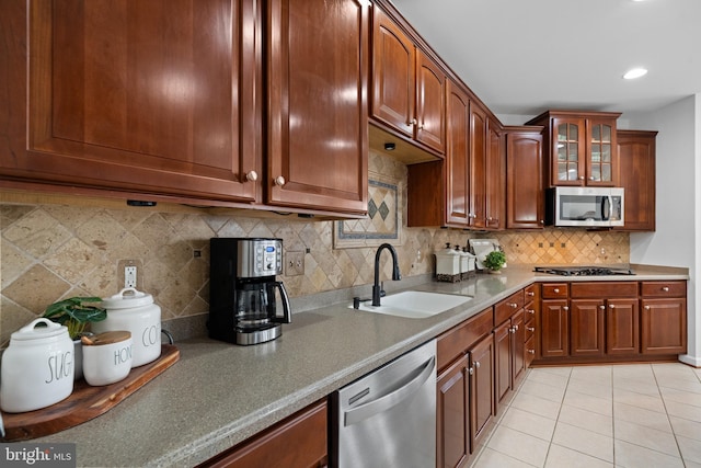 kitchen with a sink, tasteful backsplash, appliances with stainless steel finishes, light tile patterned flooring, and glass insert cabinets