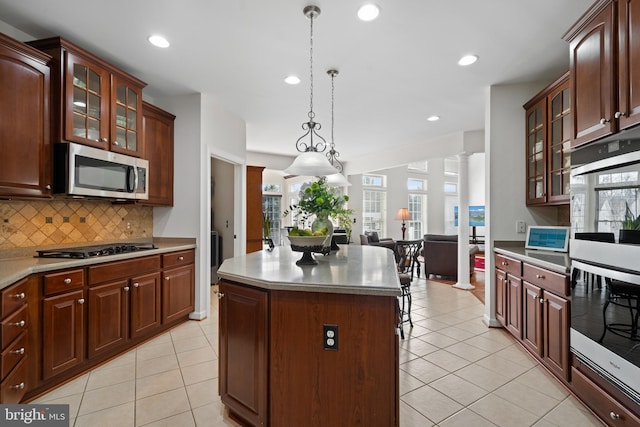 kitchen with stainless steel microwave, a kitchen island, double oven, decorative backsplash, and gas stovetop