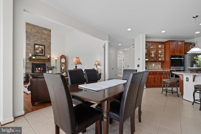 dining space featuring light tile patterned floors, a stone fireplace, recessed lighting, and ornate columns