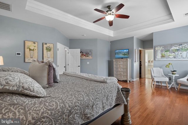 bedroom featuring wood finished floors, baseboards, visible vents, ornamental molding, and a raised ceiling