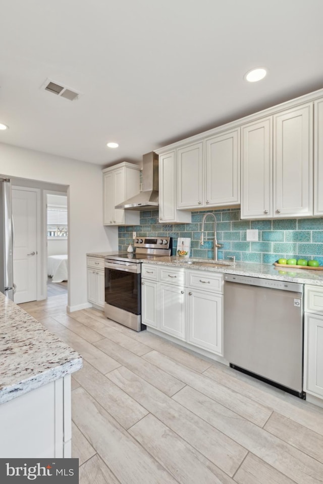 kitchen featuring white cabinetry, appliances with stainless steel finishes, sink, and wall chimney range hood