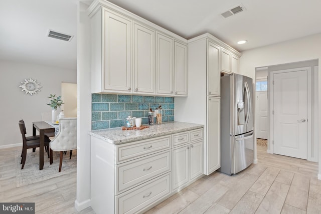 kitchen featuring stainless steel refrigerator with ice dispenser, white cabinetry, light stone countertops, light hardwood / wood-style floors, and backsplash