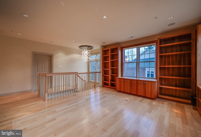 spare room with an inviting chandelier and light hardwood / wood-style floors