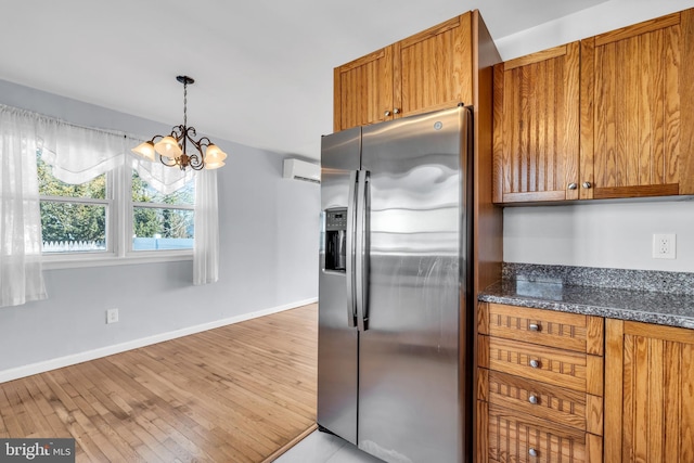 kitchen featuring a wall mounted air conditioner, stainless steel fridge with ice dispenser, light hardwood / wood-style flooring, an inviting chandelier, and dark stone countertops