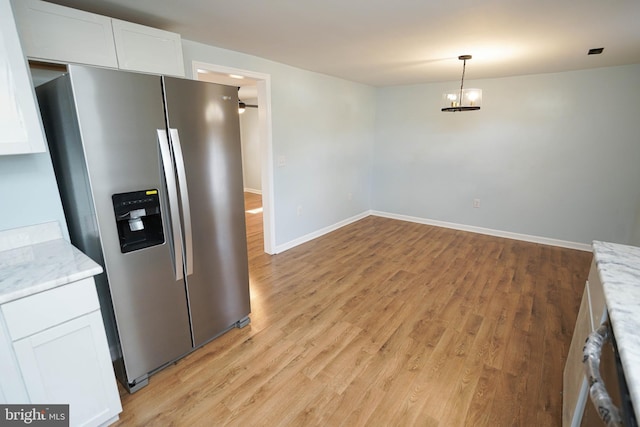 kitchen with light hardwood / wood-style floors, light stone countertops, white cabinets, stainless steel fridge with ice dispenser, and decorative light fixtures