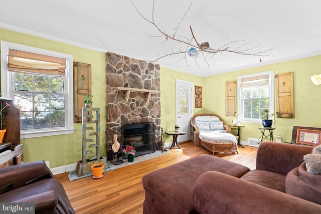 living room with crown molding, a stone fireplace, and hardwood / wood-style floors