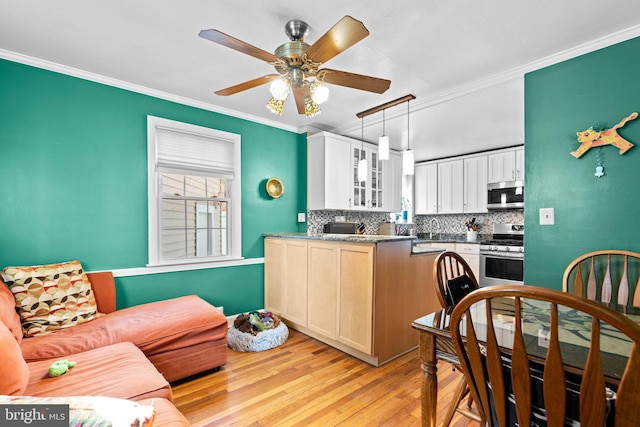 kitchen with appliances with stainless steel finishes, white cabinetry, backsplash, ornamental molding, and light hardwood / wood-style flooring