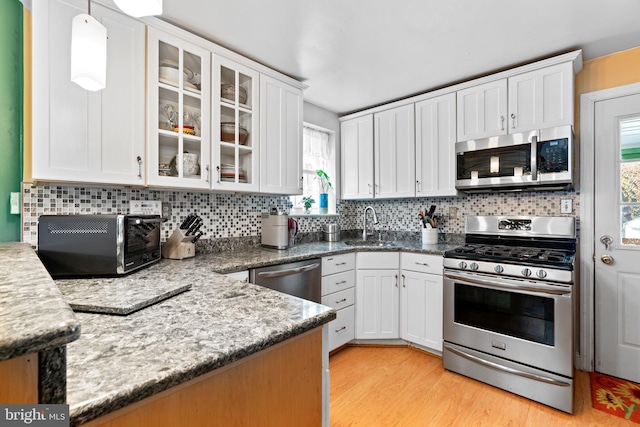 kitchen featuring appliances with stainless steel finishes, white cabinetry, hanging light fixtures, tasteful backsplash, and light hardwood / wood-style floors