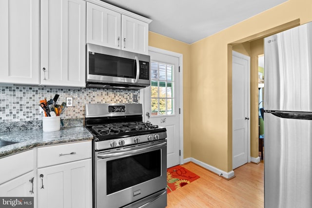 kitchen with dark stone countertops, stainless steel appliances, light hardwood / wood-style floors, decorative backsplash, and white cabinets