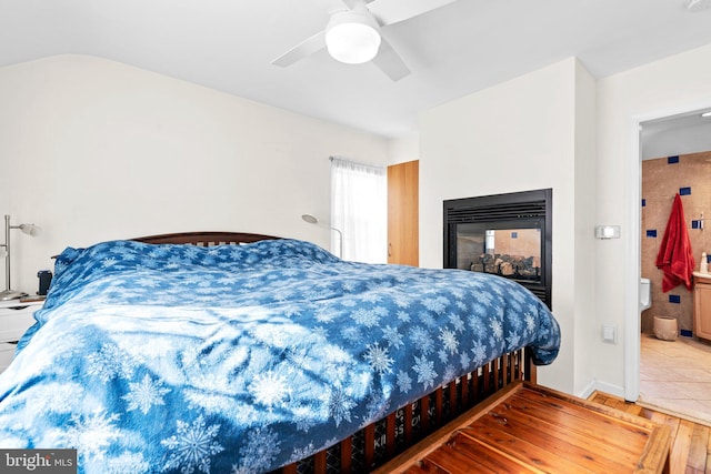 bedroom featuring connected bathroom, light hardwood / wood-style floors, ceiling fan, and a multi sided fireplace