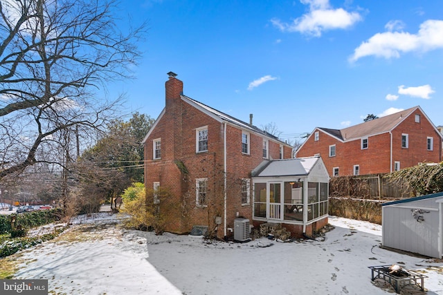 snow covered back of property featuring a sunroom, central air condition unit, and an outdoor fire pit