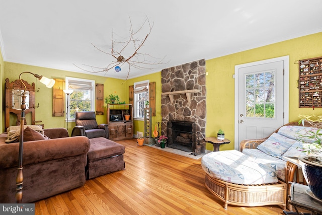 living room with crown molding, a stone fireplace, and hardwood / wood-style floors