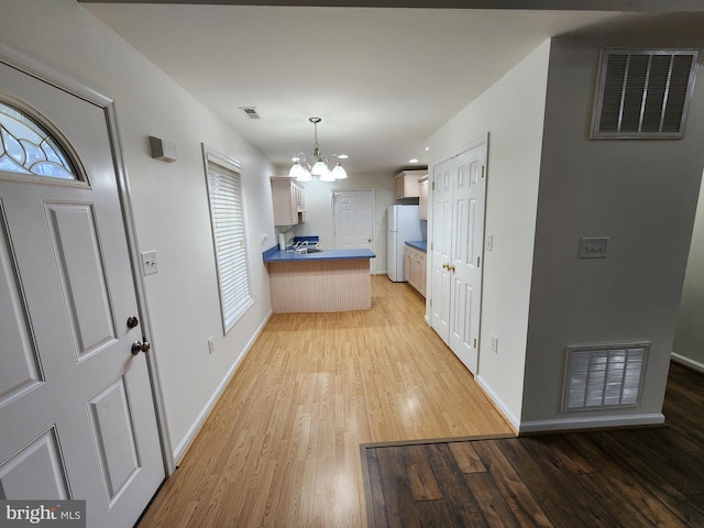 kitchen with kitchen peninsula, hanging light fixtures, light hardwood / wood-style flooring, white refrigerator, and an inviting chandelier