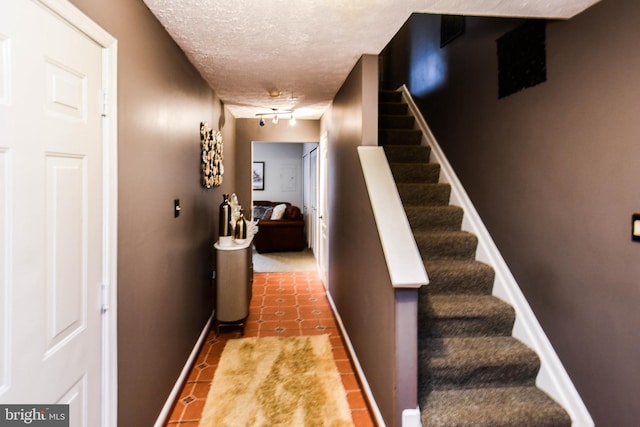 hall featuring tile patterned flooring, track lighting, and a textured ceiling