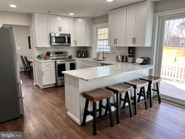 kitchen with sink, white cabinets, a kitchen breakfast bar, kitchen peninsula, and stainless steel appliances