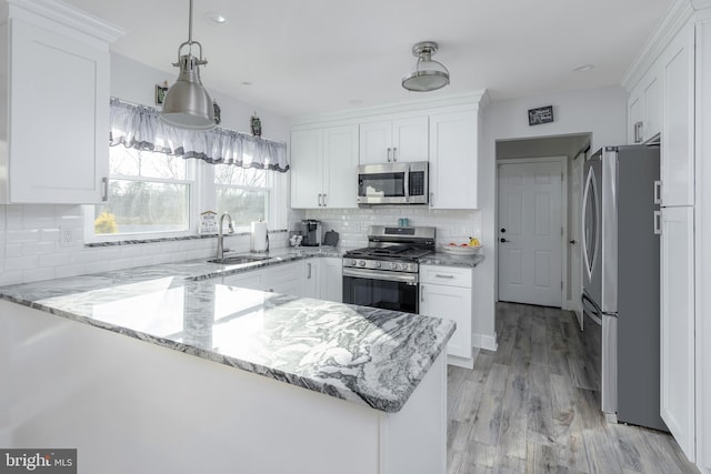 kitchen featuring sink, light stone counters, appliances with stainless steel finishes, kitchen peninsula, and white cabinets