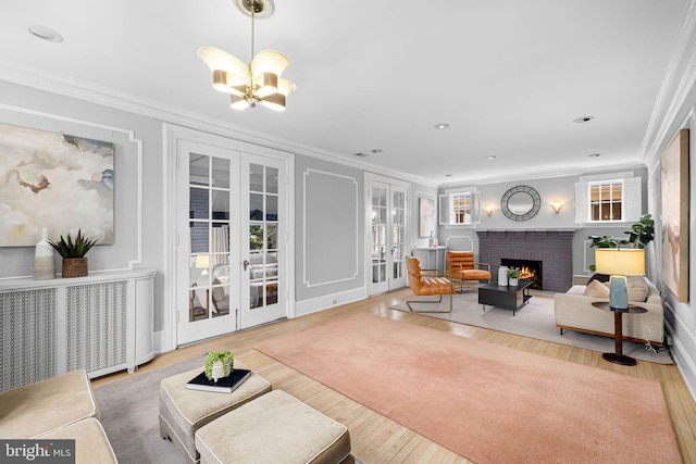 living room featuring french doors, crown molding, a brick fireplace, a notable chandelier, and hardwood / wood-style flooring