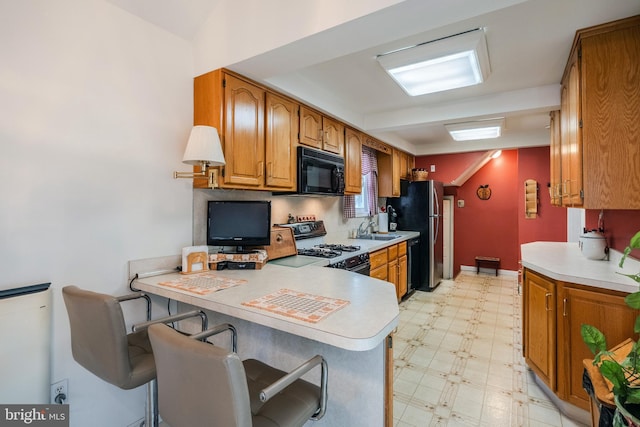 kitchen with sink, black appliances, a kitchen breakfast bar, and kitchen peninsula