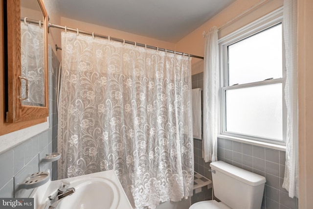 bathroom with a shower with curtain, a wealth of natural light, tile walls, and toilet