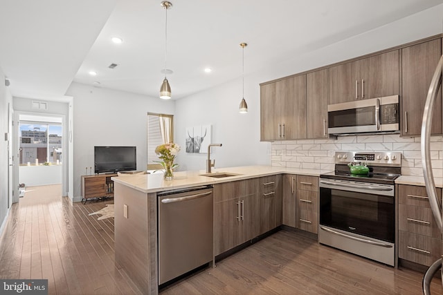 kitchen with appliances with stainless steel finishes, dark hardwood / wood-style floors, sink, hanging light fixtures, and kitchen peninsula