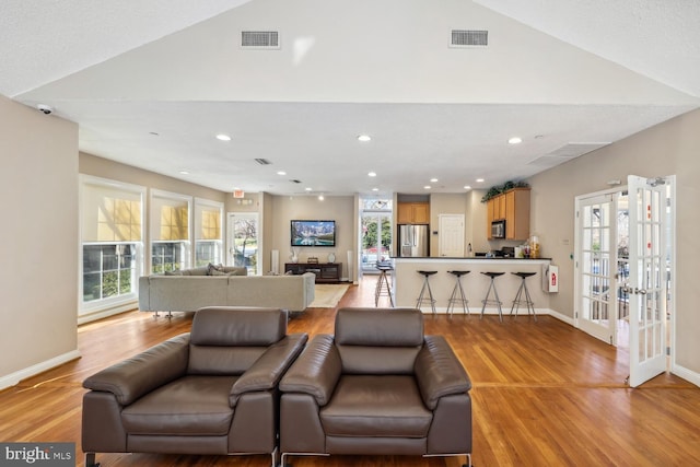 living room featuring french doors, vaulted ceiling, and light wood-type flooring