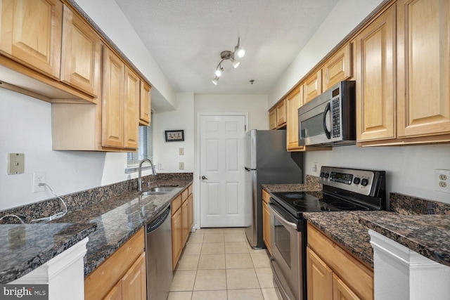 kitchen with stainless steel appliances, light tile patterned flooring, sink, and dark stone counters