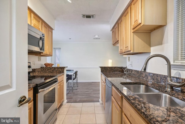 kitchen featuring light tile patterned flooring, light brown cabinetry, sink, dark stone countertops, and appliances with stainless steel finishes