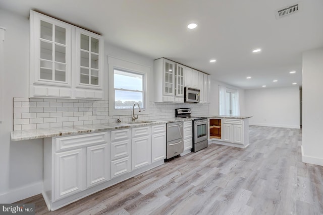 kitchen with light stone countertops, sink, backsplash, appliances with stainless steel finishes, and white cabinets