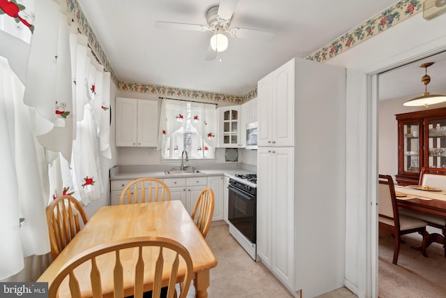 kitchen with a sink, white appliances, white cabinets, light countertops, and glass insert cabinets