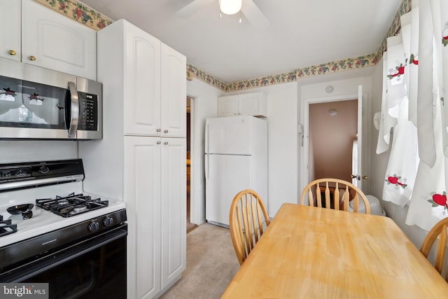 kitchen with stainless steel microwave, gas range oven, freestanding refrigerator, white cabinetry, and a ceiling fan