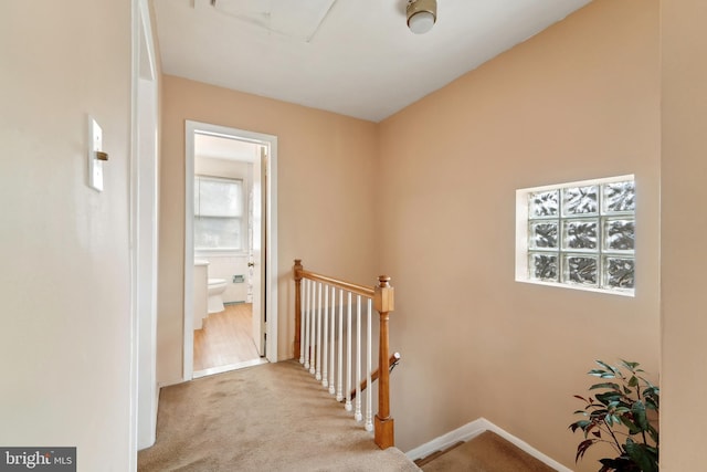 hallway with an upstairs landing, baseboards, and carpet