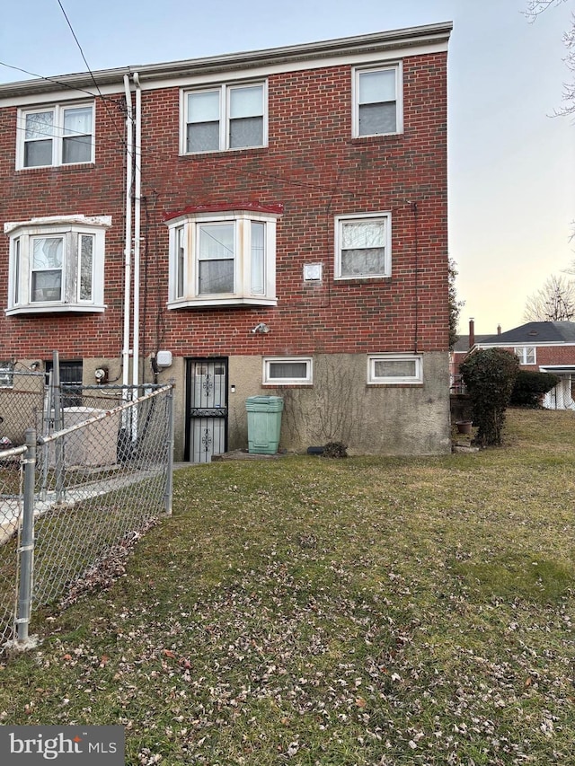 rear view of house with fence, a lawn, and brick siding