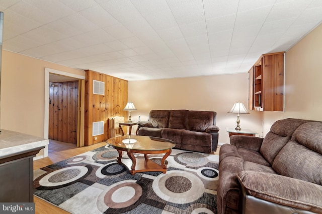 living room with visible vents, wood walls, and light wood-style floors