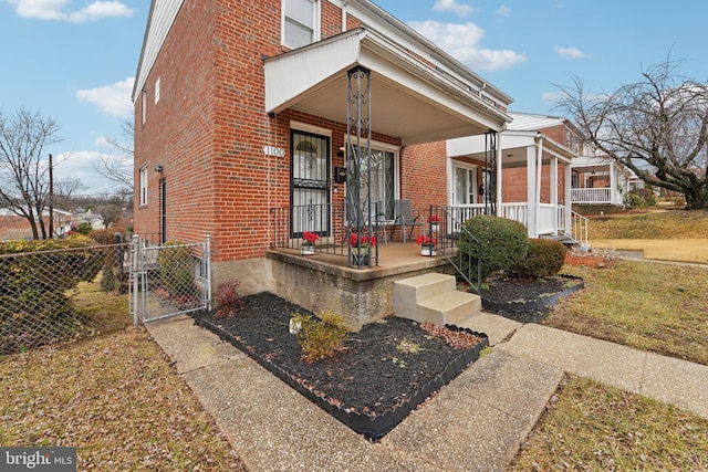 view of exterior entry with brick siding, covered porch, and a gate