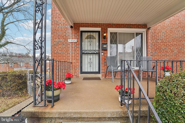 property entrance featuring a porch, fence, and brick siding