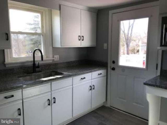 kitchen with dark hardwood / wood-style flooring, sink, dark stone counters, and white cabinets