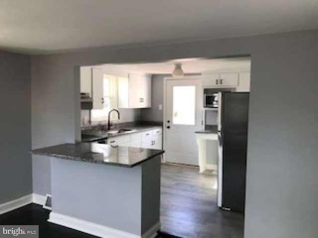 kitchen featuring sink, dark wood-type flooring, black refrigerator, white cabinetry, and kitchen peninsula