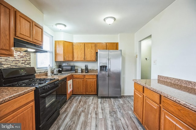 kitchen with dishwashing machine, backsplash, black gas range, light hardwood / wood-style floors, and stainless steel fridge