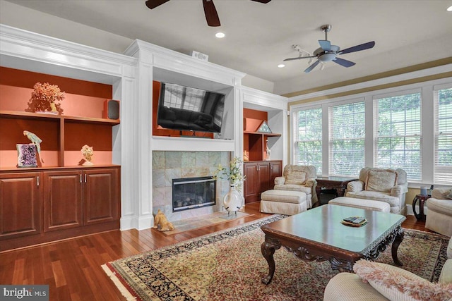 living room with a tiled fireplace, plenty of natural light, dark hardwood / wood-style flooring, and built in shelves