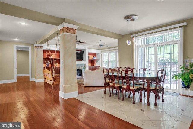 dining space featuring ornate columns, ceiling fan, a fireplace, and light hardwood / wood-style floors