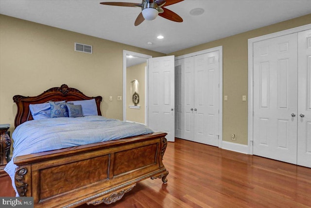 bedroom featuring ceiling fan, wood-type flooring, and two closets