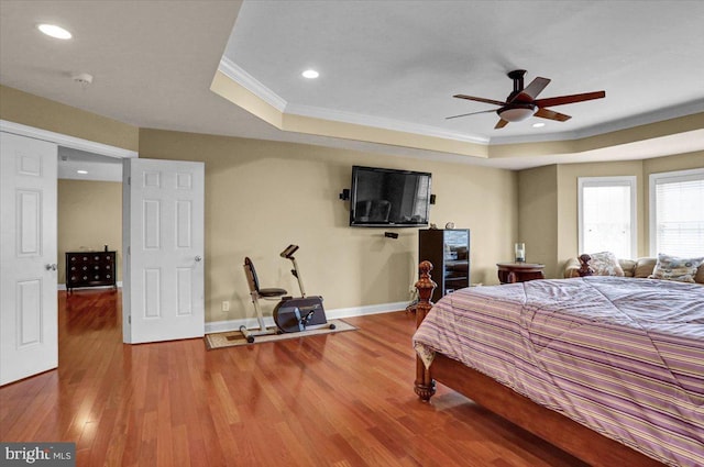 bedroom with hardwood / wood-style flooring, ceiling fan, a tray ceiling, and crown molding