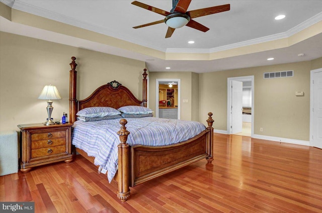 bedroom with ensuite bathroom, hardwood / wood-style flooring, ceiling fan, a tray ceiling, and crown molding