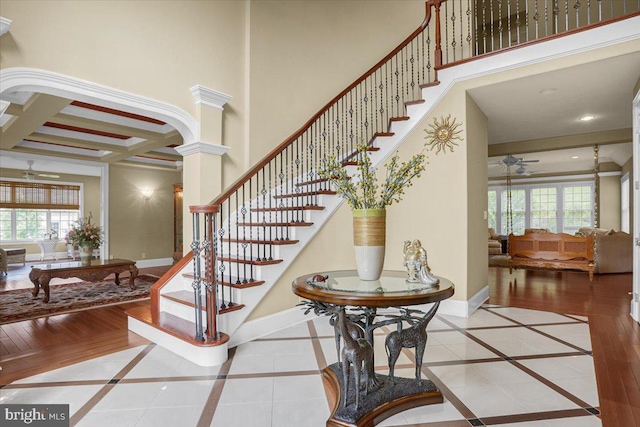 staircase with coffered ceiling, beamed ceiling, ceiling fan, decorative columns, and a high ceiling