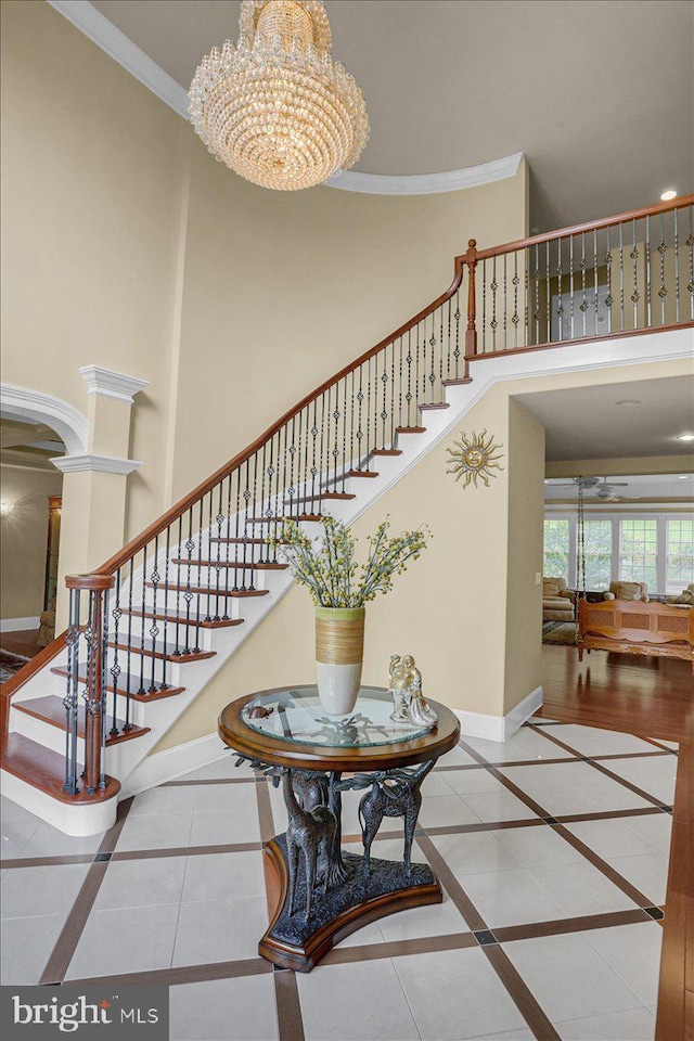 stairs with ornate columns, ornamental molding, a notable chandelier, a towering ceiling, and tile patterned flooring